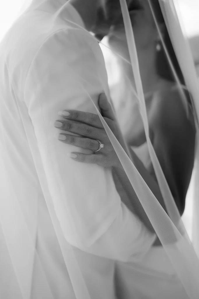 Black and white detail of a bride’s hand with an engagement ring on the groom’s arm as they embrace under a sheer veil in Opatija, Croatia